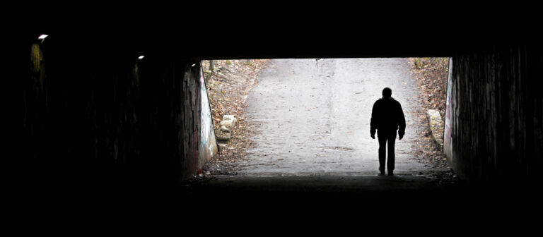 Silhouette eines Mannes im dunklen Tunnel, am Ende sieht man eine Straße im Licht, die bergauf führt.