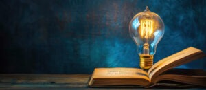 Aufgeschlagenes Buch vor einem dunklen Hintergrund, darüber eine leuchtende Glühbrine.
