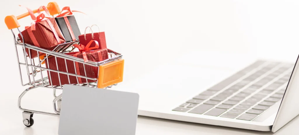 Mini-Einkaufswagen mit Geschenken neben Laptop
