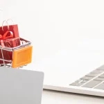 Mini-Einkaufswagen mit Geschenken neben Laptop