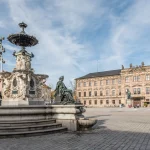Prunkvoller Brunnen vor barockem Schloss auf historischem Platz